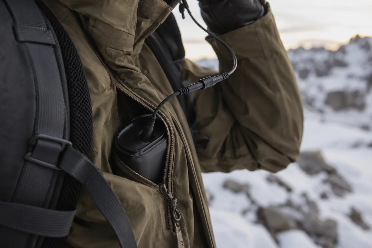 Nahaufnahme eines Stirnlampen-Verlängerungskabels zu einem Akkupack in einer Jackentasche, Schnee im Hintergrund